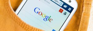 A mobile phone is hanging out of a yellow jean pocket with Google showing on the screen