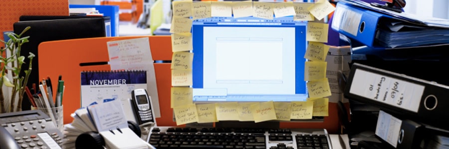 A computer monitor with post-it notes surrounding it on a messy desk