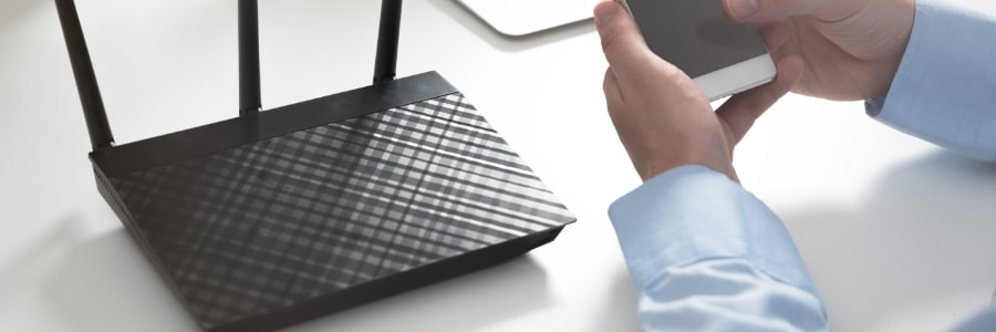 A router is on a table whilst a pair of hands is holding a mobile phone away from it