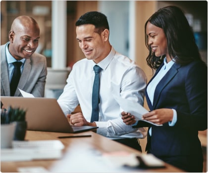 Three people in business wear looking at a laptop screen